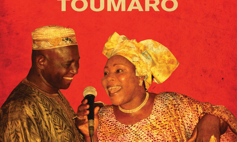 Hawa & Kasse Mady Diabaté – Toumaro. Portada del disco con el padre e hija alrededor de un micrófono, con fondo rojo.